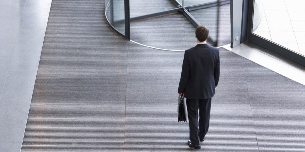 Business professional walking into an office building, representing workforce changes and rehiring after redundancy